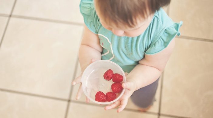 toddler holding a bowl of raspberry