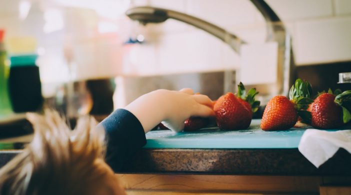 small boy reaching for strawberries by kitchen sink