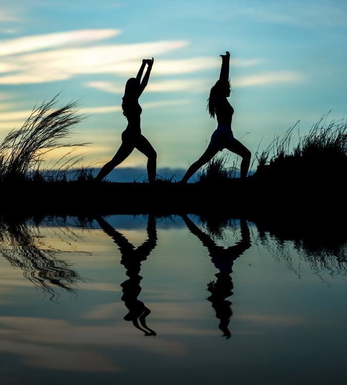 two women striking a yoga pose near a body of water