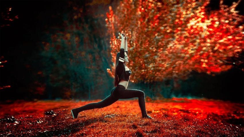woman doing yoga with arms stretched toward the sky near a bright red tree