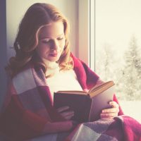 happy girl reading a book by the window in the winter